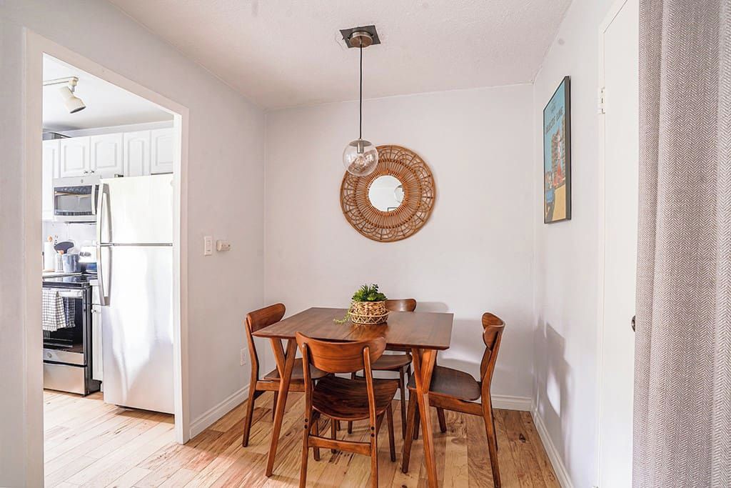 A compact dining area with a wooden table and chairs, a hanging light fixture, and a woven wall decoration.