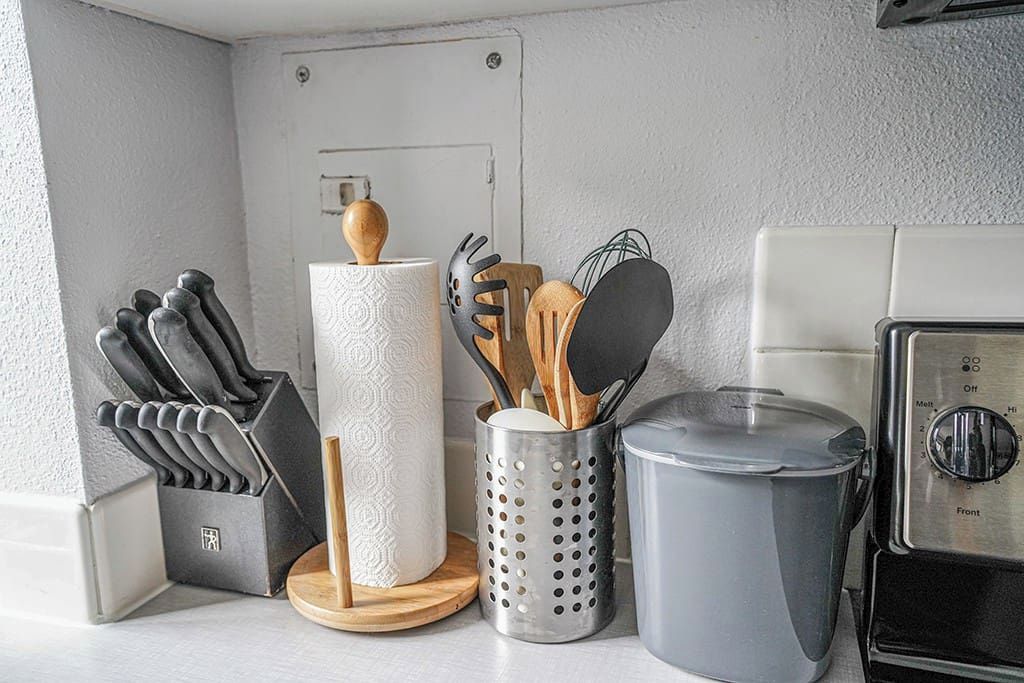 Eine Küchenarbeitsplatte mit einem Messerblock, einem Papierhandtuchhalter, einem Sieb und einem Toaster.