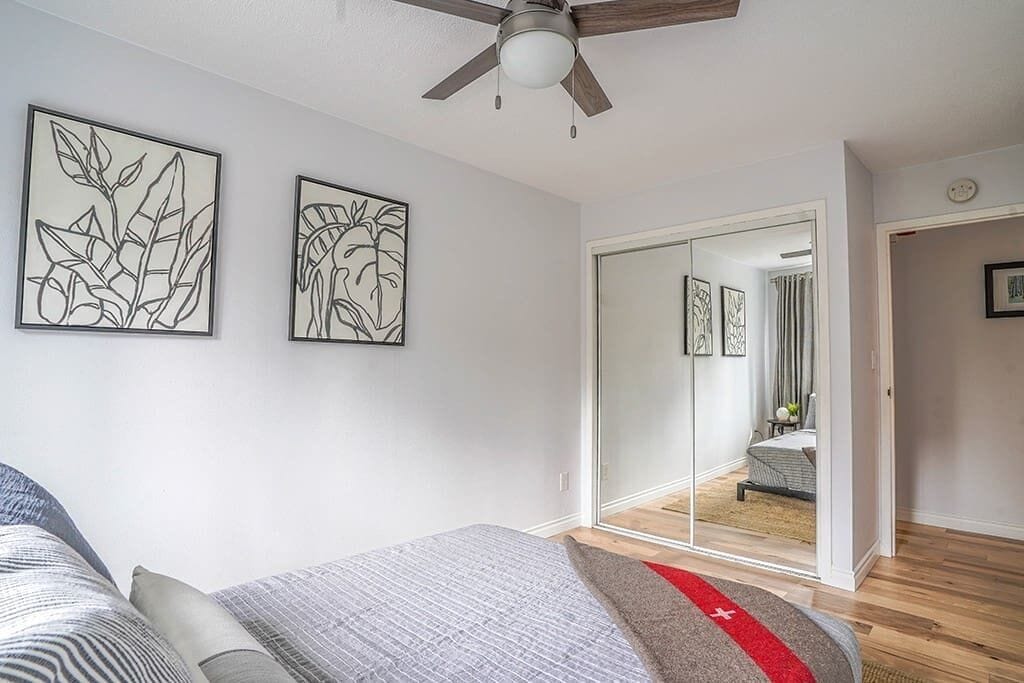 A bedroom with a bed, a ceiling fan, and two framed wall art pieces.