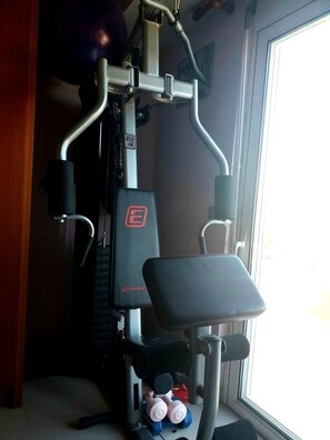 Ein Heimfitnessraum mit einem Ergometer, einer Langhantelbank und Kurzhanteln.