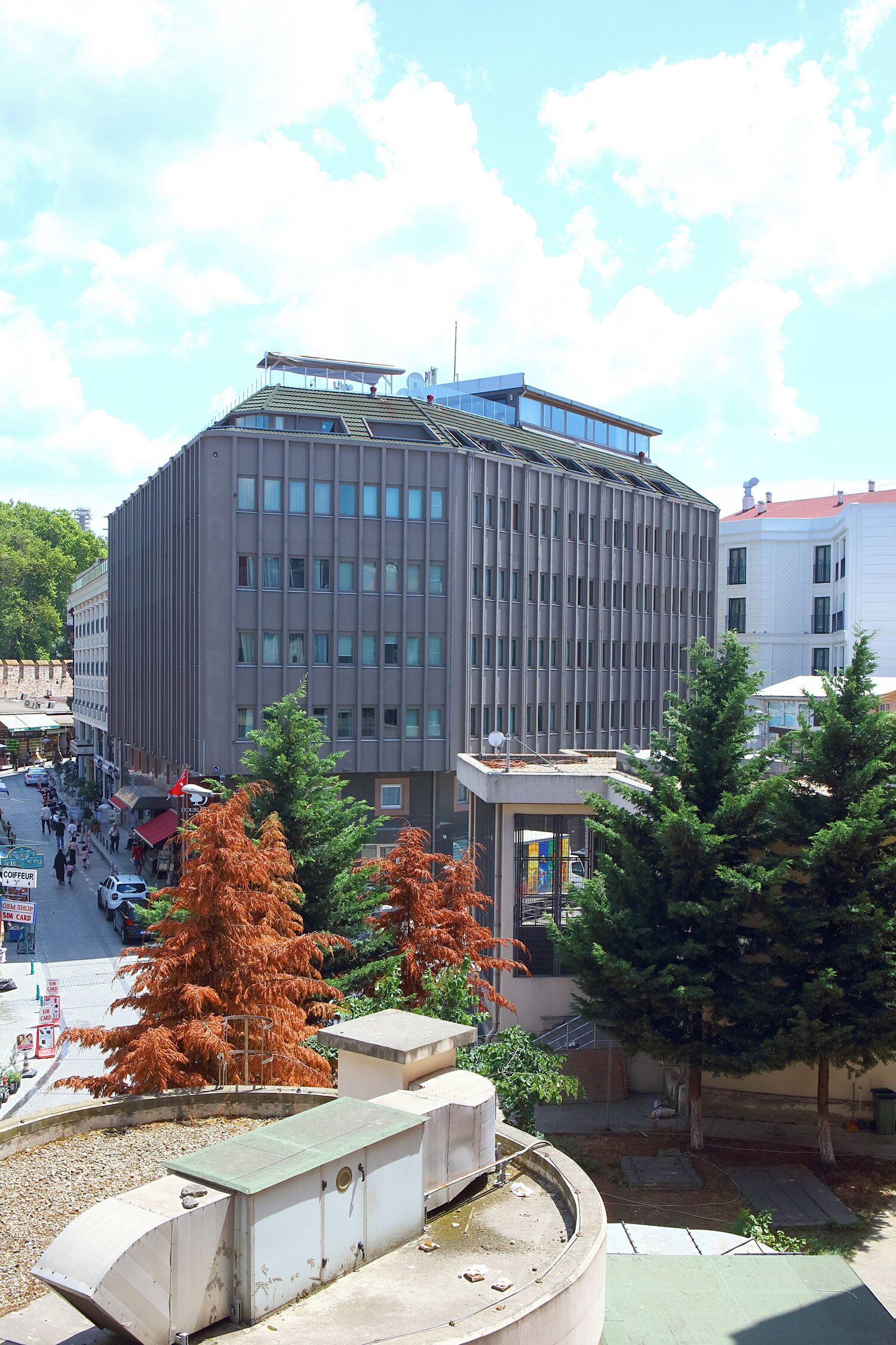 A modern building with a curved facade, a rooftop terrace, and a small garden area with trees.
