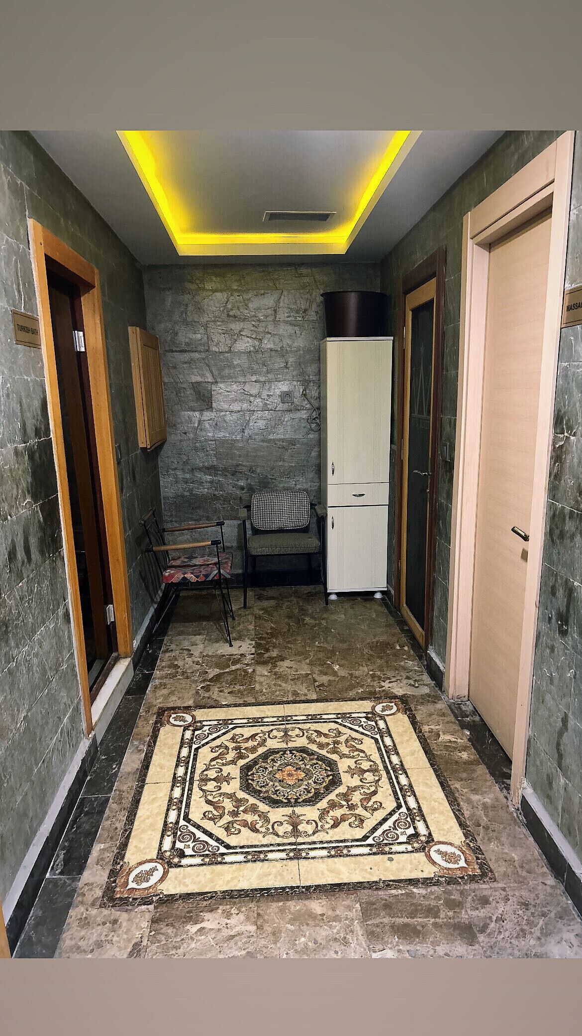 Un pasillo con alfombra estampada, paredes de piedra y una lámpara en el techo.