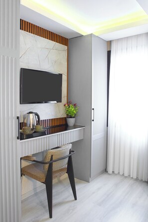 Una habitación moderna con un televisor montado en la pared, una mesita con hervidor, tazas y una planta en maceta, además de una silla.