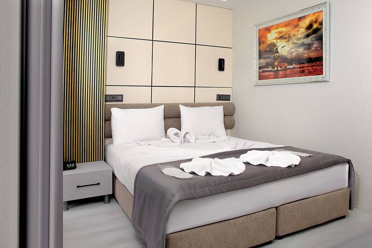 A neatly made bed with white linens and a gray blanket, a bedside table with a phone, and a framed picture of a sunset over water on the wall.