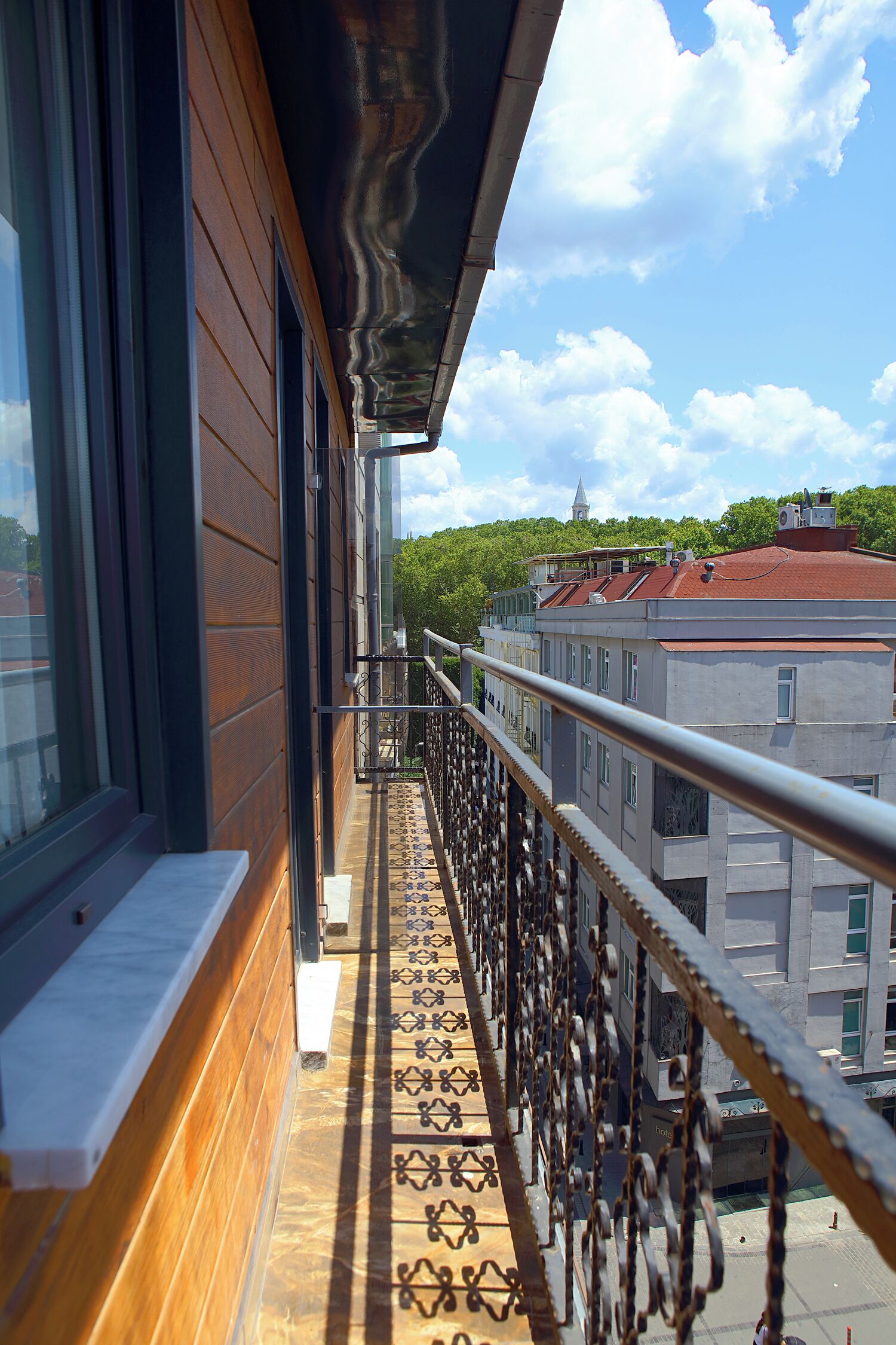 A balcony with a patterned floor, a metal railing, and a view of buildings and trees in the background.
