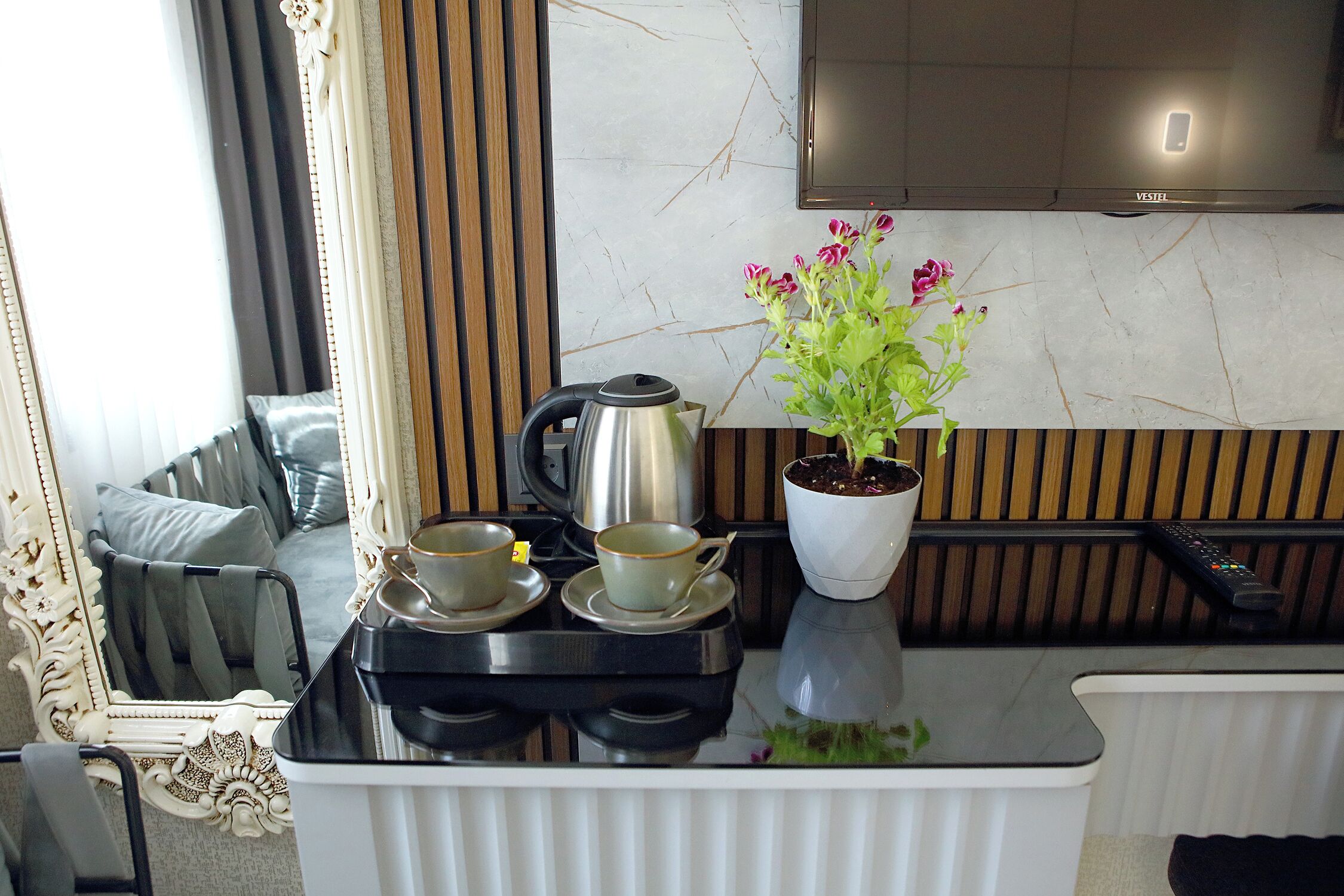 A kitchen with a stove, kettle, cups, a potted plant, and a TV.