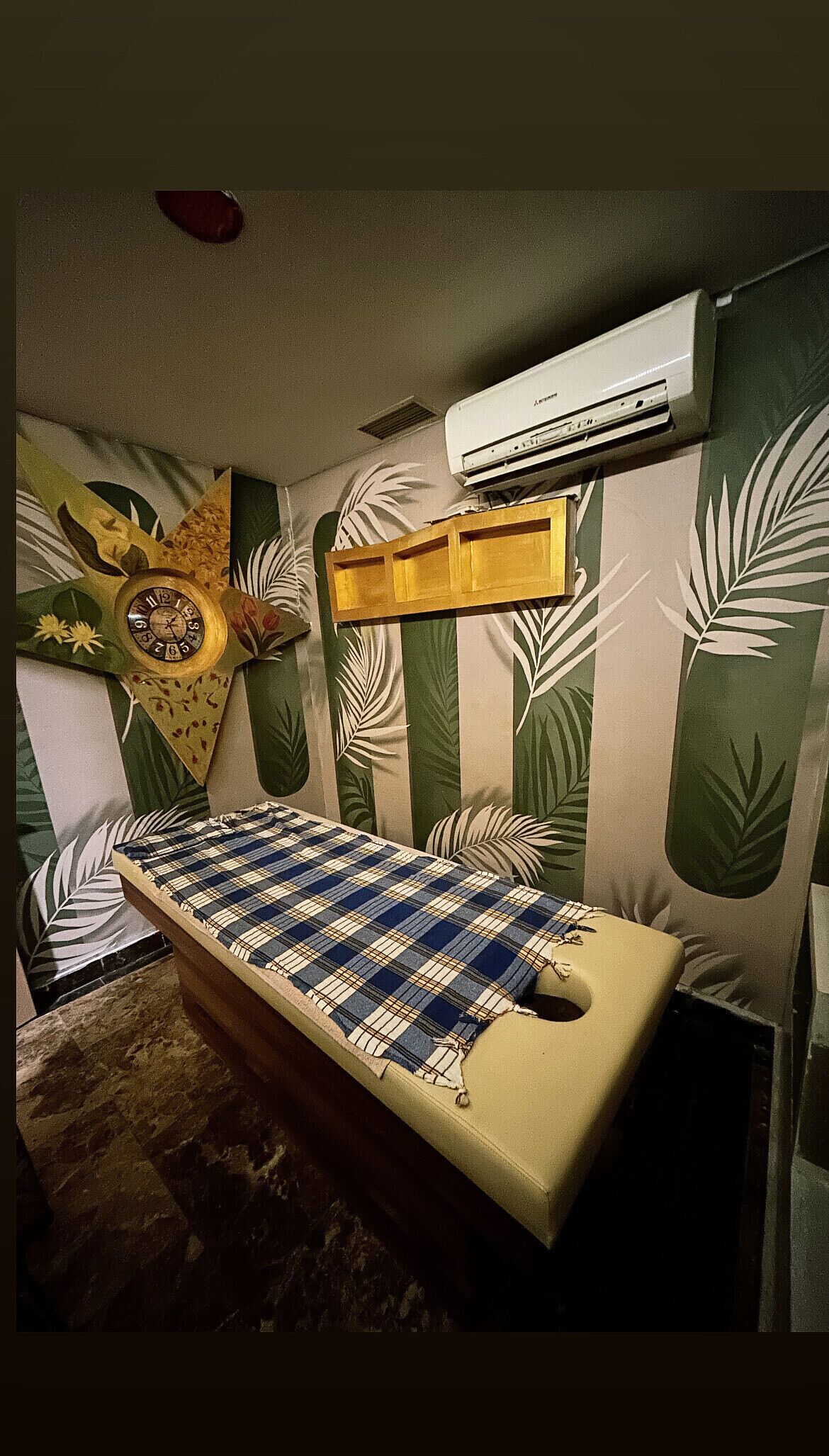 A room with a bed, a wall clock, and an air conditioning unit.