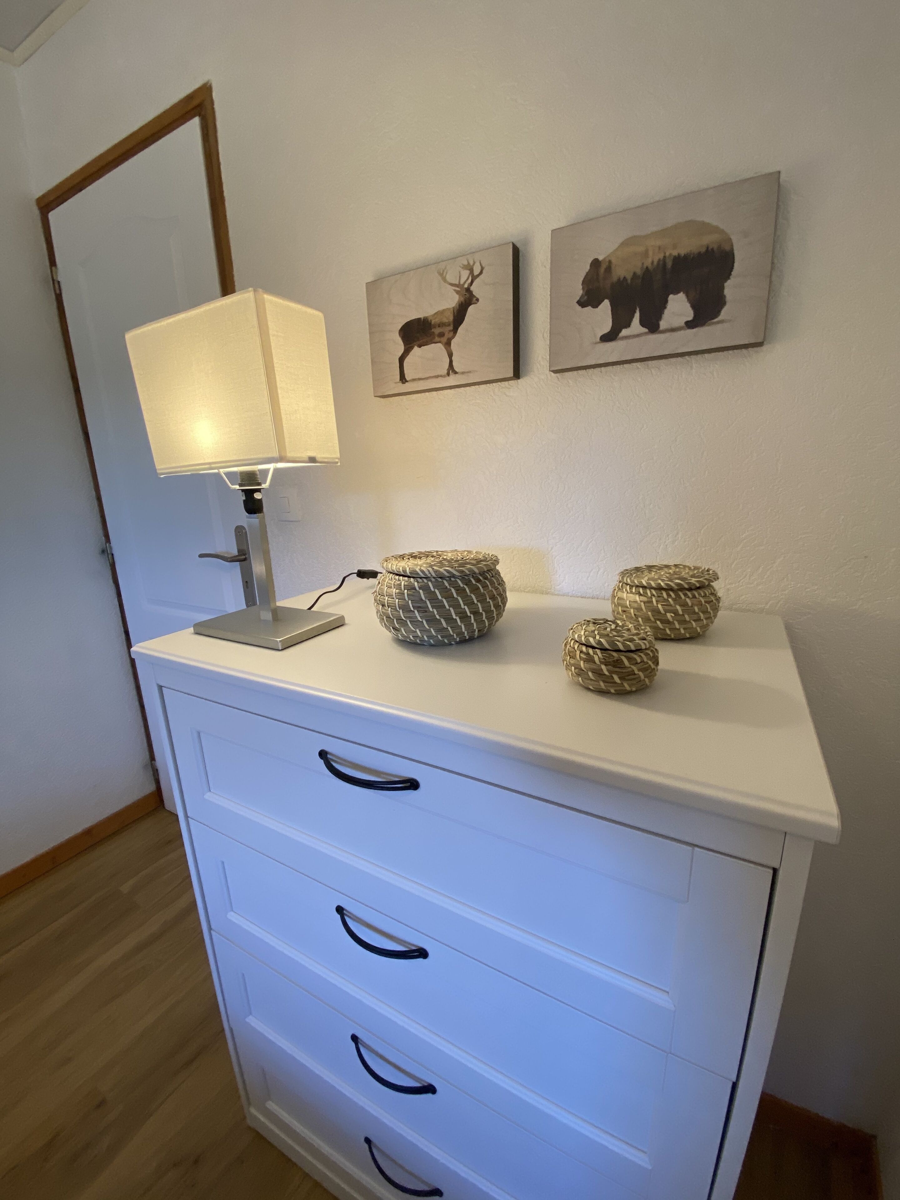 En vit byrå med tre lådor och en lampa ovanpå. Ovanför byrån hänger två inramade bilder med djurmotiv.