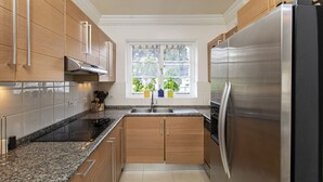 A modern kitchen with wooden cabinets, a stainless steel refrigerator, and a window with plants. - The Falls Villa No. 1 | Elegant Caribbean Retreat in Holetown (Holetown)