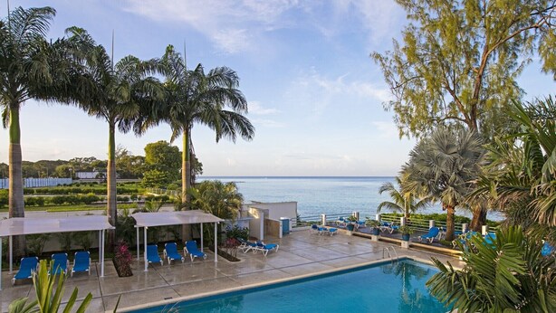 A pool area with blue lounge chairs, a covered seating area, and a view of the sea. - The Falls Villa No. 1 | Elegant Caribbean Retreat in Holetown (Holetown)