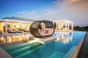 Une piscine à débordement moderne, dotée d’un fauteuil lounge sphérique original et d’un espace extérieur bien éclairé.