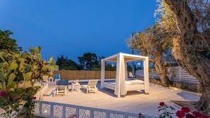 En privat udendørs patio med himmelseng, liggestole og et lille bord.