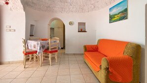 A room with a dining table, chairs, a sofa, a painting, and a kitchen visible through an archway. - Holiday Home 'Trulli da Rosy' with Private Garden & Terrace (Martina Franca)