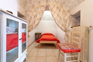 Une chambre à coucher avec un lit, une chaise en bois, une armoire et une fenêtre avec des rideaux.