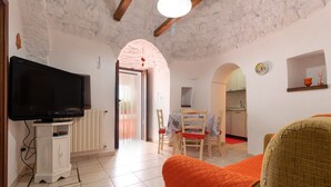 A living room with a television, a dining area with chairs, a kitchen in the background, and a staircase leading to an upper floor. - Holiday Home 'Trulli da Rosy' with Private Garden & Terrace (Martina Franca)