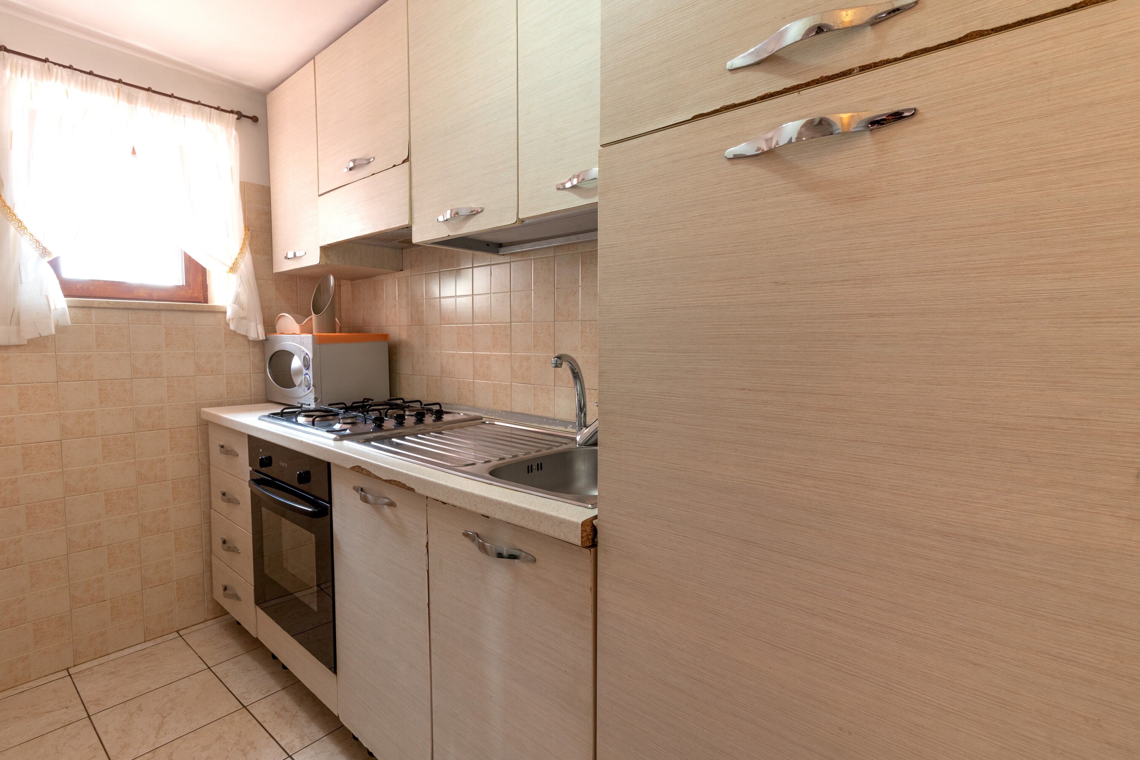 Une cuisine de taille réduite, équipée d’une cuisinière à gaz, d’un four, d’un évier et de meubles de rangement de couleur claire.