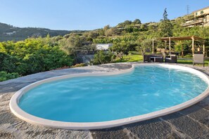 Ein Schwimmbecken mit Steinrand, umgeben von einem Garten und einer Pergola mit Sitzgelegenheiten.