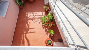 Un balcon carrelé, agrémenté de plantes en pot et doté d’une rambarde en métal.