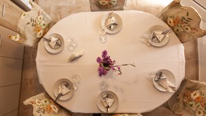 Une table ronde dressée pour six personnes, avec des chaises à motifs floraux, un vase rempli de fleurs violettes et une nappe blanche.