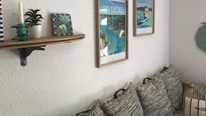 Eine Wand mit zwei gerahmten Postern, ein Regal mit Dekoration und eine Sitzecke mit Kissen.