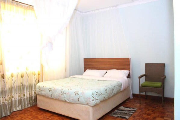 A bedroom with a bed, a chair, and a window with curtains. - Tribu Guesthouse Nakuru (Nakuru)