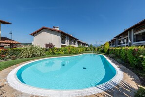 Piscina rodeada por um jardim ajardinado, com um edifício ao fundo.