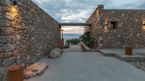 Ein Steinhäuschen mit Blick auf das Meer, ein Betonweg und eine hölzerne Bank.
