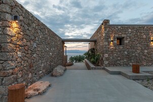 A stone building with a view of the sea, a concrete pathway, and a wooden bench.