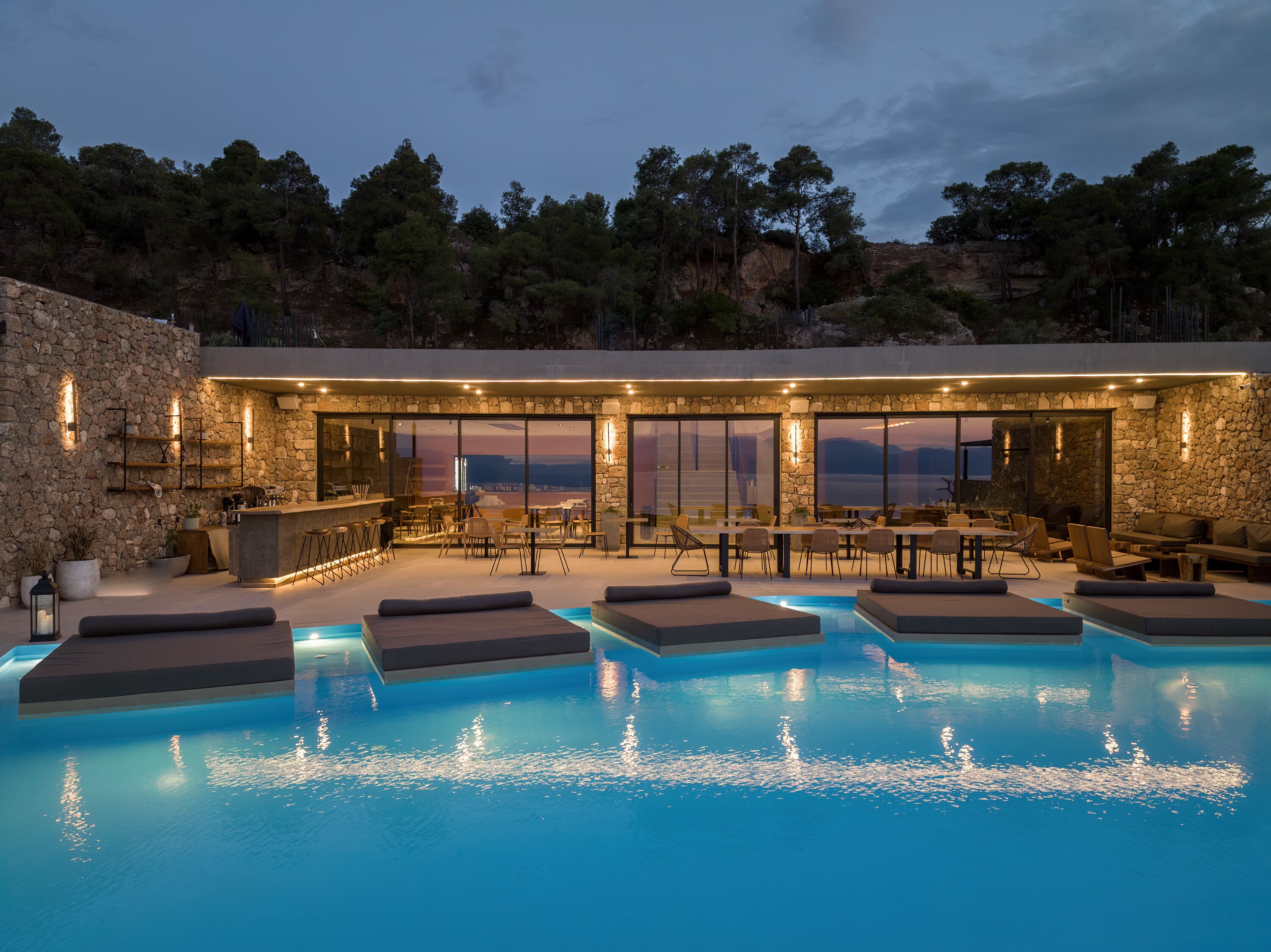 A modern outdoor pool area with stone walls, bar, and seating.