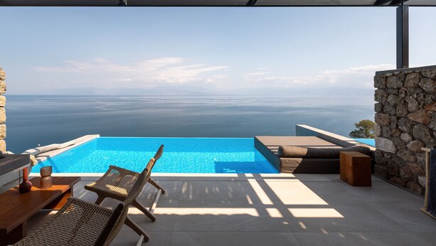 Une piscine à débordement offrant une vue dégagée sur la mer, des chaises longues et un mur en pierre.