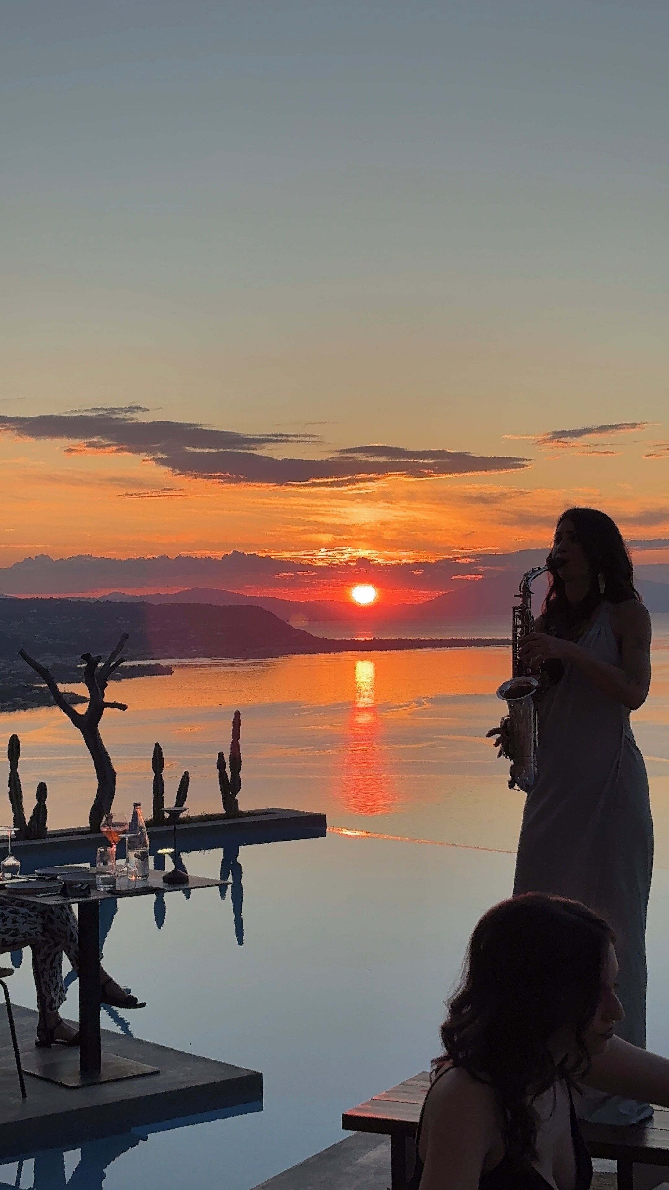 Una persona suona il sassofono a un tavolo sul lago al tramonto.