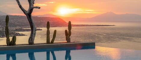 Ein Fernblick von einem Infinity-Pool auf einen Sonnenuntergang über Wasser und Berge.