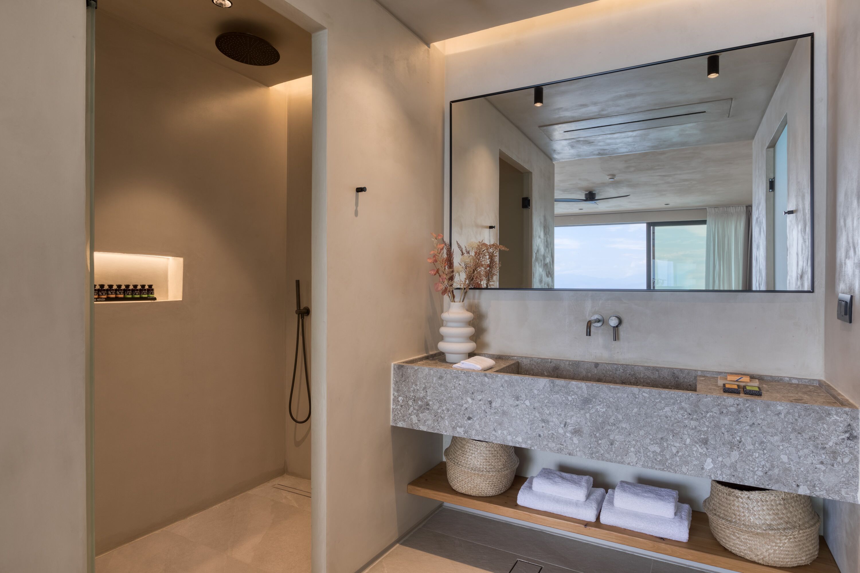 A modern bathroom with a large mirror, a granite countertop, and a shower area.