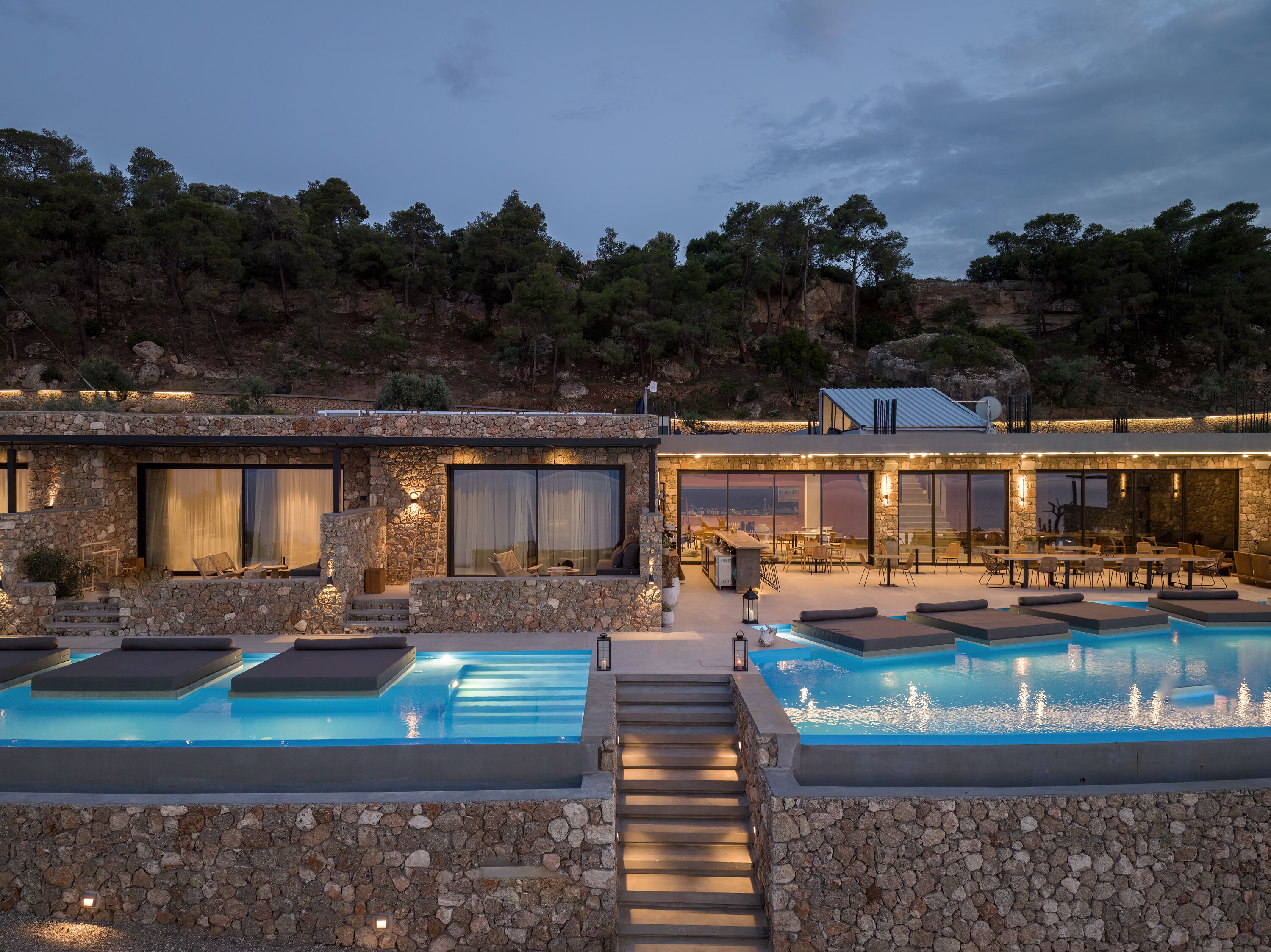 A modern resort with a pool area, stone walls, and a dining area with outdoor seating.