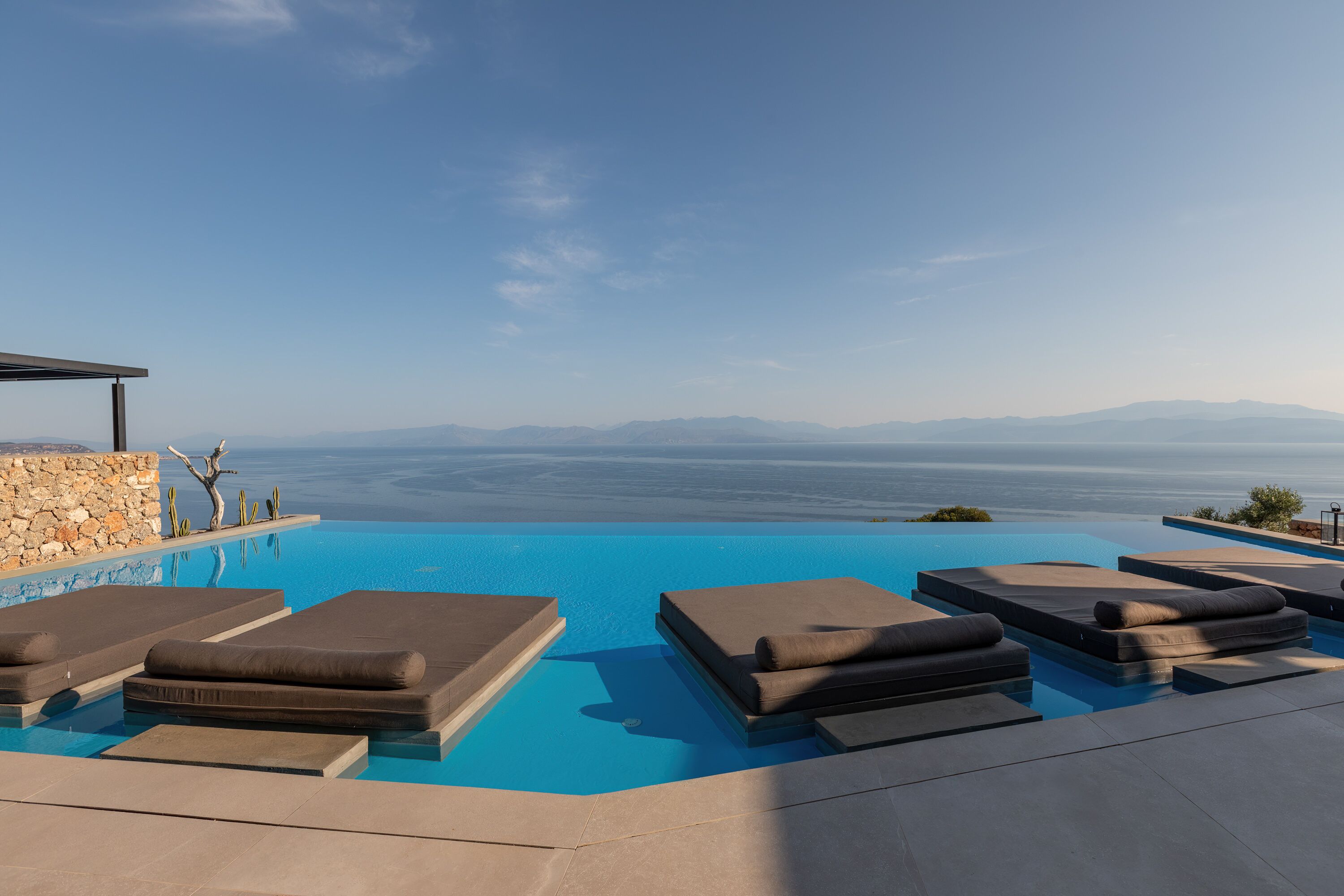 Una piscina infinita con sillones de descanso y un muro de piedra.