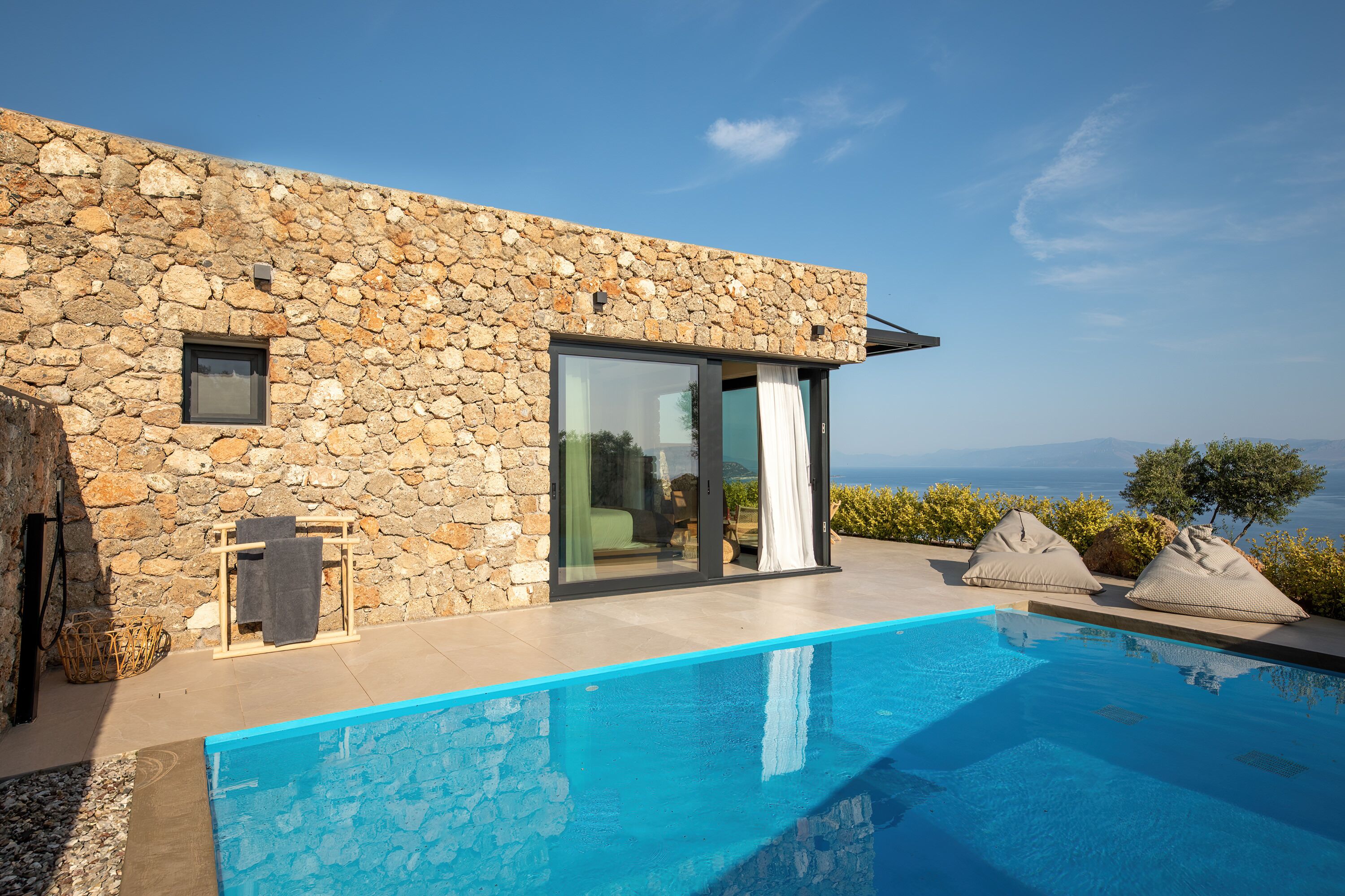 A modern stone building with a pool, large sliding glass doors, and a view of the sea.