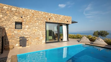 A modern stone building with a pool, large sliding glass doors, and a view of the sea.