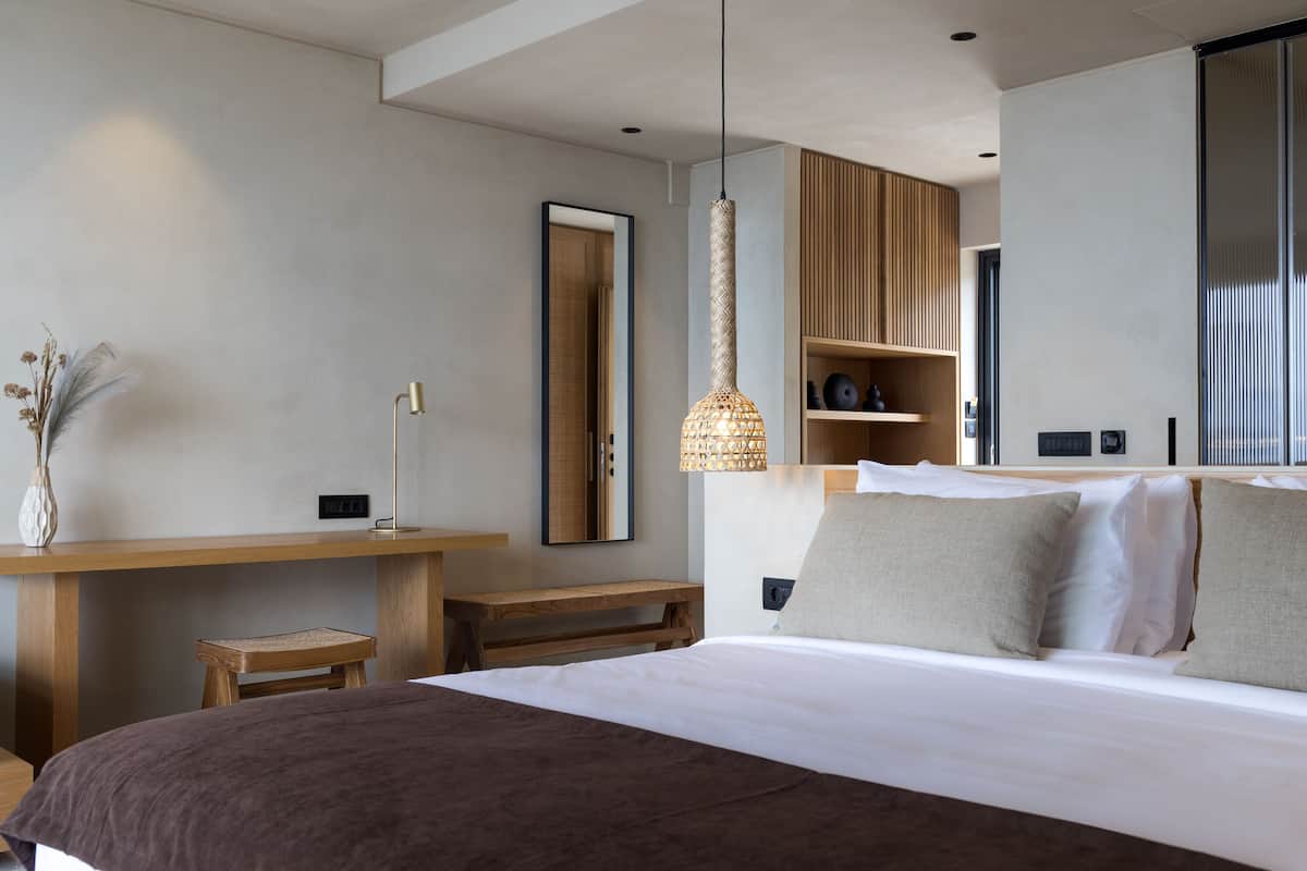 Una habitación de hotel moderna con una cama grande, un escritorio de madera, un taburete pequeño y una lámpara colgante.