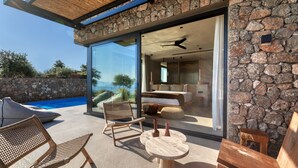 Ein moderner Außenbereich mit Korbstühlen und einem Holztisch, mit Blick auf einen Swimmingpool und eine Steinmauer.