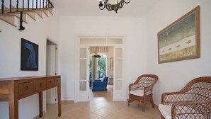 A spacious living area with a wooden console table, wicker furniture, a blue sofa, and a painting on the wall. - Casa Can Alou, authentic Mallorquin house nestled in the village of Porto Colom (Felanitx)