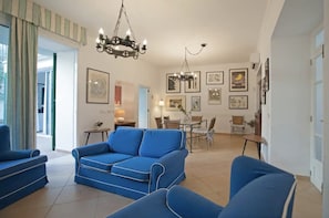 A living room with a blue sofa, a dining area with a table and chairs, and a chandelier. - Casa Can Alou, authentic Mallorquin house nestled in the village of Porto Colom (Felanitx)