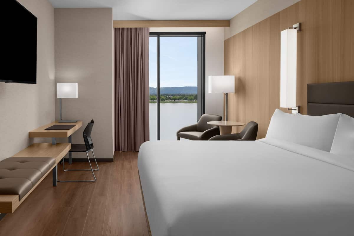 A modern hotel room with a large bed, a desk with a chair, a small table, and a TV.