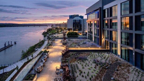 A modern building with a rooftop garden and seating area overlooking a river.