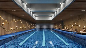 Una piscina interior moderna con suelo de baldosas azules, paneles de madera y sillones de descanso a lo largo de los bordes.