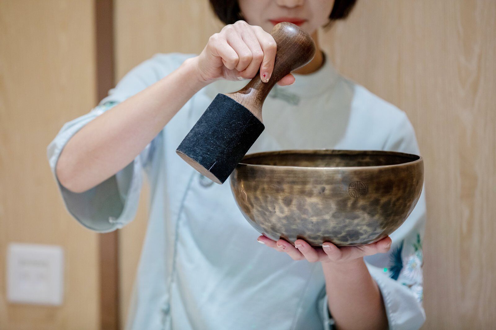 A person holding a metallic bowl with a wooden mallet.