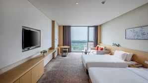 Habitación de hotel con dos camas, televisor, escritorio y vistas a la ciudad.