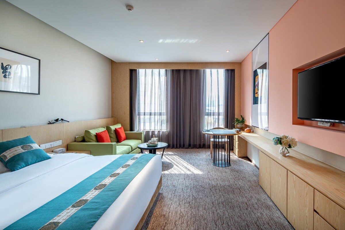 A hotel room with a bed, a sofa, a small table, a TV, and a window with curtains.