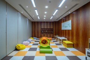Uma sala de brinquedos com piso xadrez, tapetes de atividades, puffs e um túnel de brincadeira.
