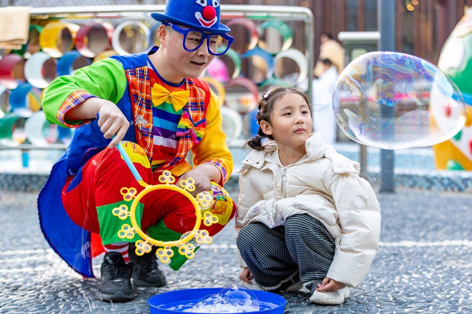 A child and an adult playing with bubbles outdoors.