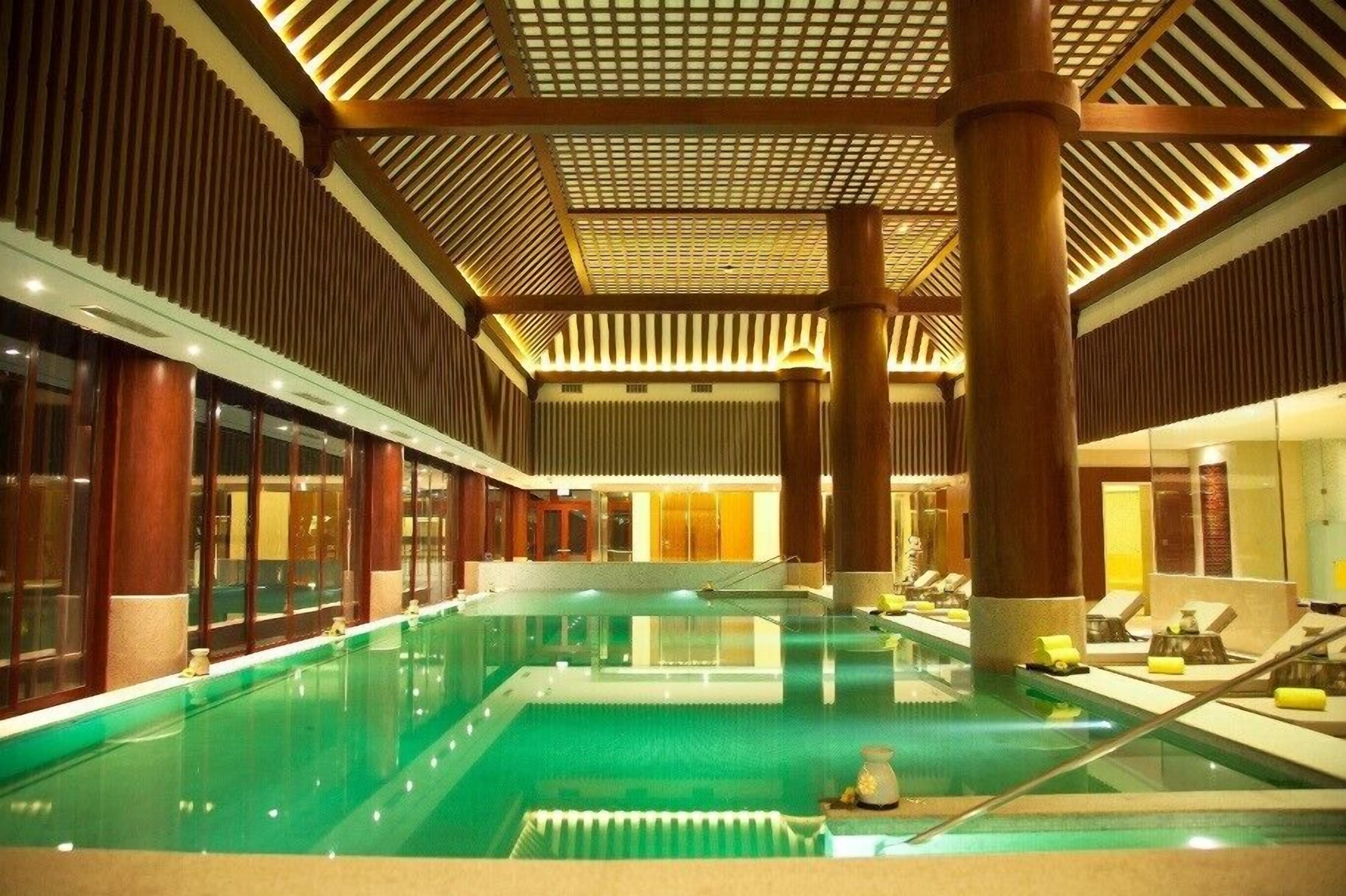 An indoor swimming pool with a modern design, surrounded by lounge areas and wooden paneling.